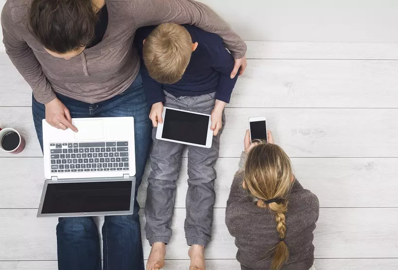 Family of three looking into laptop, tablet and phone