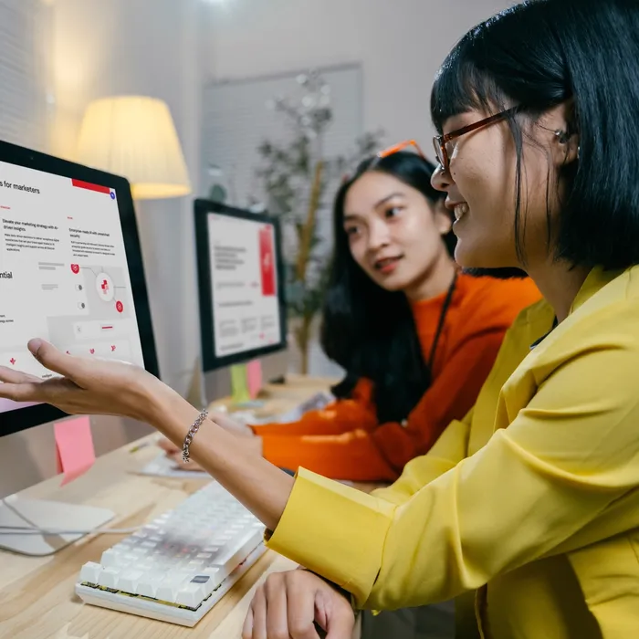 woman in yellow shirt talking with another woman in front of computers in the office 