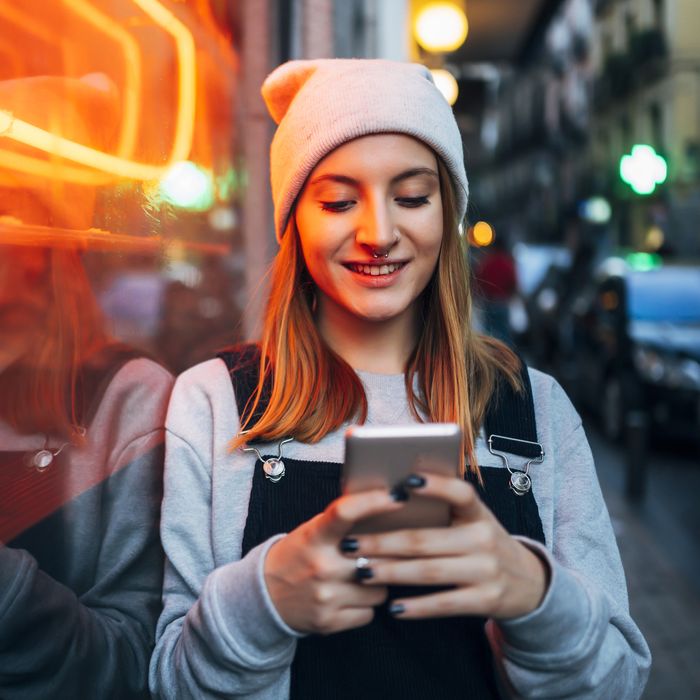 Smiling young woman standing next to neon light using her smartphone at night