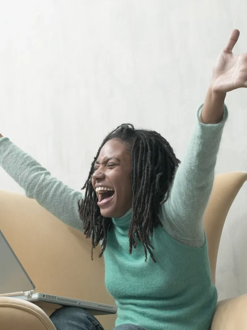 Young woman, sitting in armchair with laptop, arms outstretched