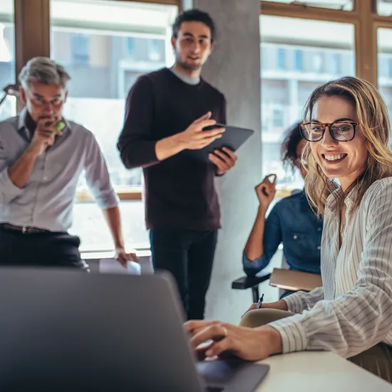 Female entrepreneur working on laptop and explaining strategy to attract followers to online web store while having meeting with colleagues in office.