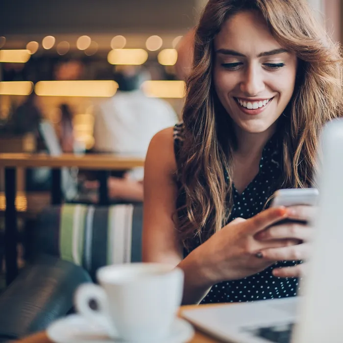 Smiling young woman with laptop and smart phone sitting in cafeteria, with copy space