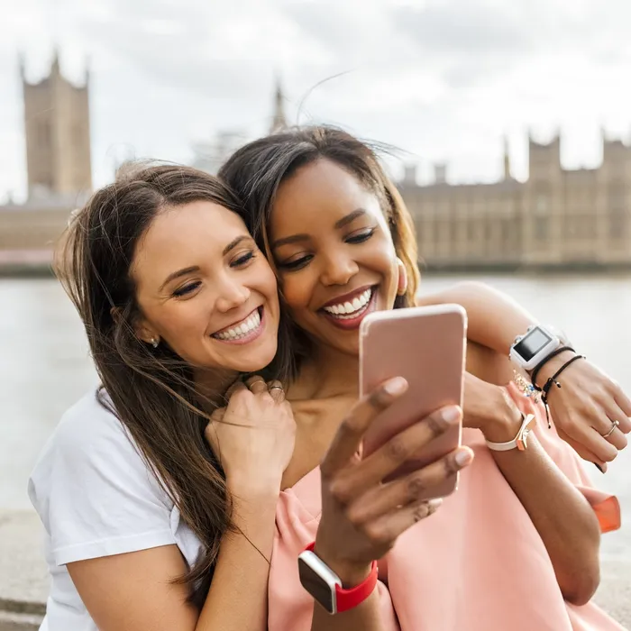 UK, London, two happy women with smartphone near Westminster Bridge