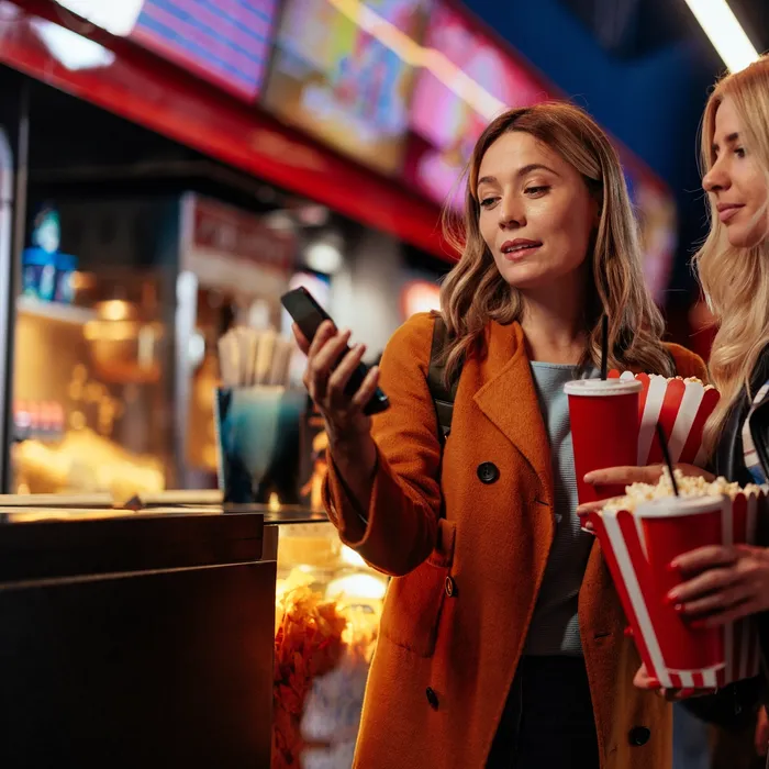 two women in cinema holding popcorns and phone 