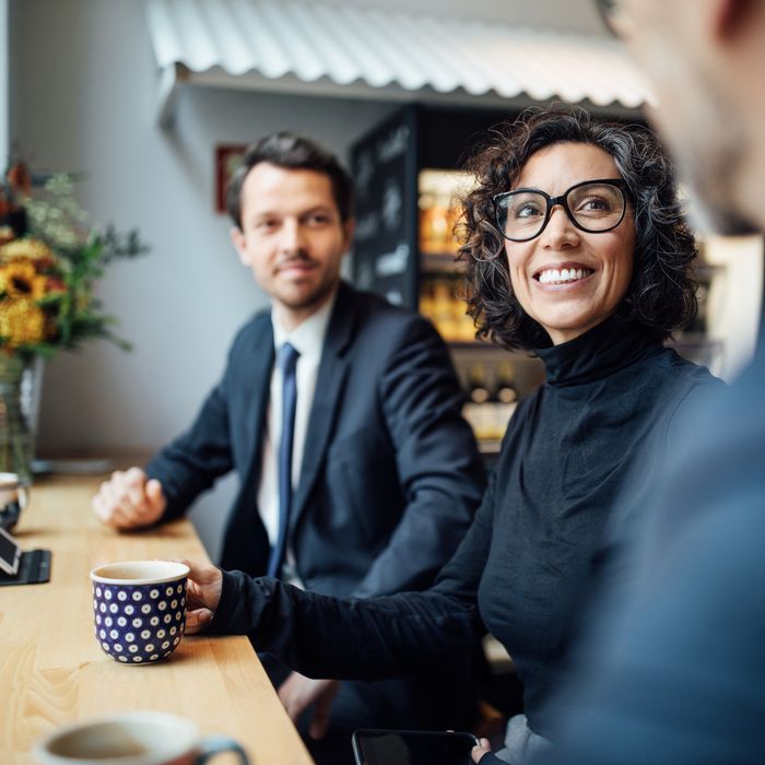 Mature woman sitting amongst colleagues at coffee shop. Group of three business people sitting at a coffee shop and talking.