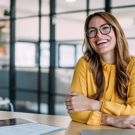 Portrait of a beautiful smiling businesswoman sitting on desk in her office and looking at camera.