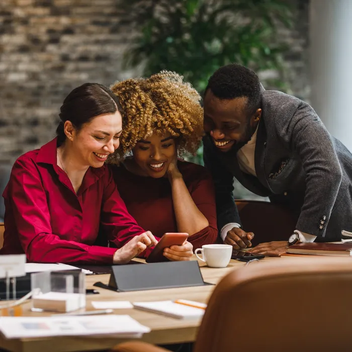 Copy space shot of three diverse business colleagues hanging out during coffee break and laughing at funny memes they are viewing via smart phone.Colorful Human