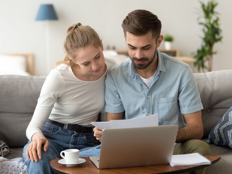 a man and a woman are sitting on a sofa looking at documents and laptop on the table