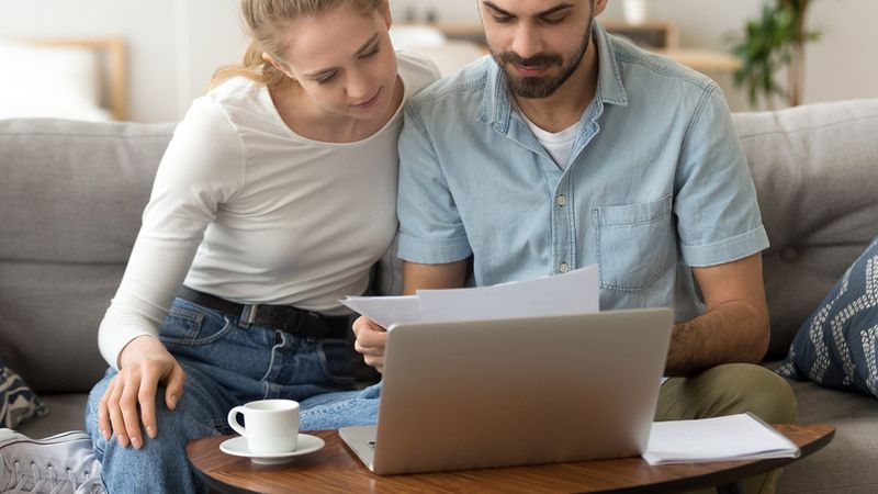 a man and a woman are sitting on a sofa looking at documents and laptop on the table