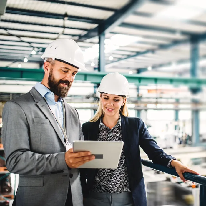A portrait of an industrial man and woman engineer with tablet in a factory, working. 