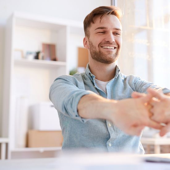 Portrait of handsome young man  stretching at workplace in office and smiling happily, copy space