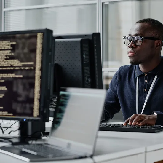 African American young developer in eyeglasses concentrating on his online work on computer sitting at workplace