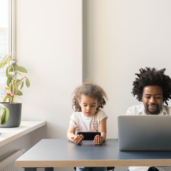 Stock Photo Of Father working from home with a laptop with his daughter near using cellphone. 