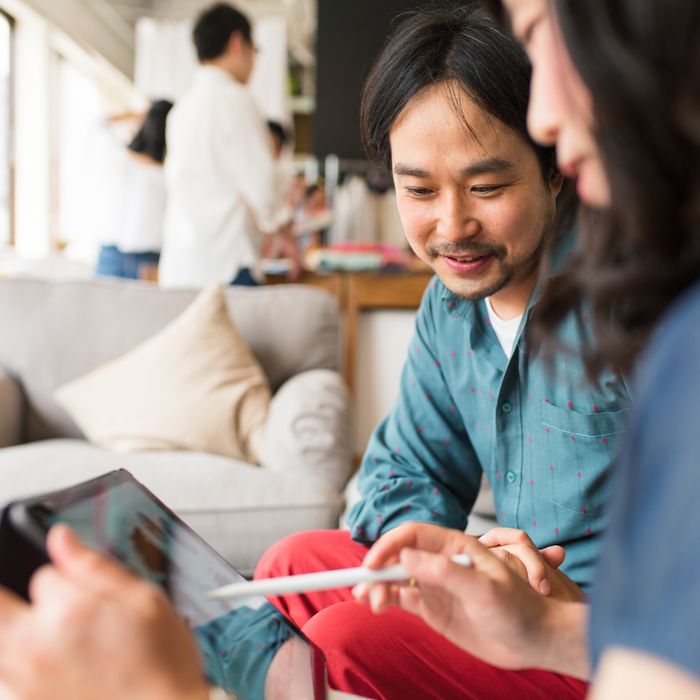 Two coworkers in casual clothes having a business meeting and looking at data on a digital tablet. Kyoto, Japan. May 2016