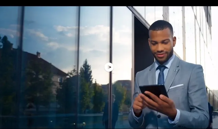 A businessman walking past a building while looking at a tablet