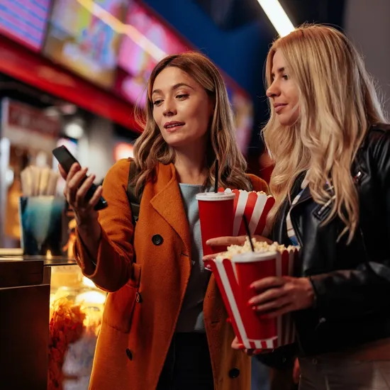 two women in cinema holding popcorns and phone 