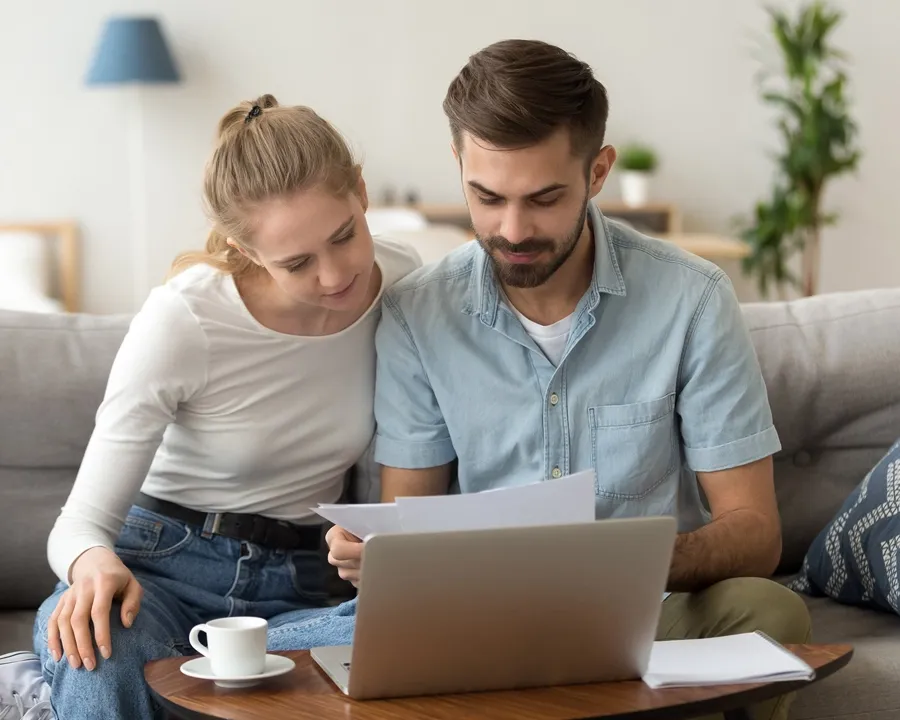a man and a woman are sitting on a sofa looking at documents and laptop on the table