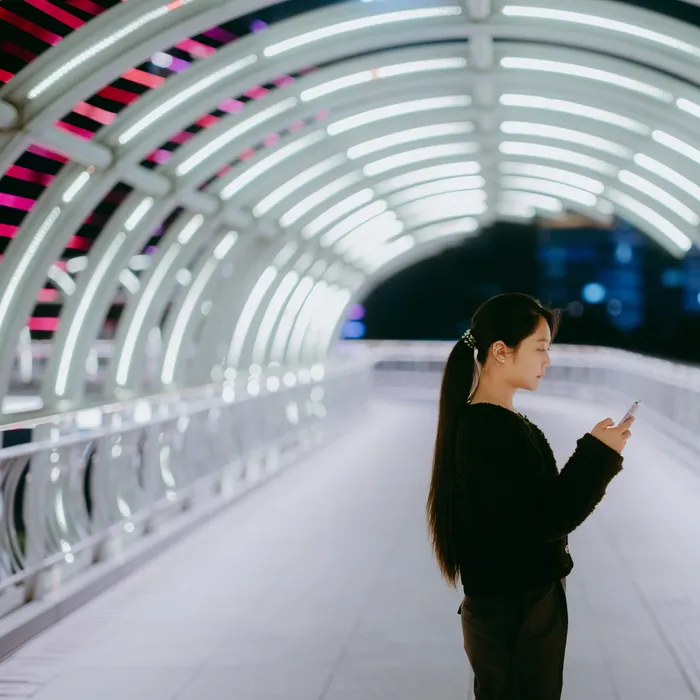 Businesswoman using smartphone on modern pedestrian bridge at nightColorful Human