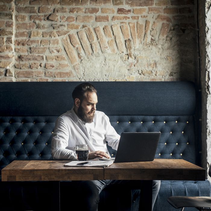 Handsome modern young Caucasian businessman reading on laptop at bar.