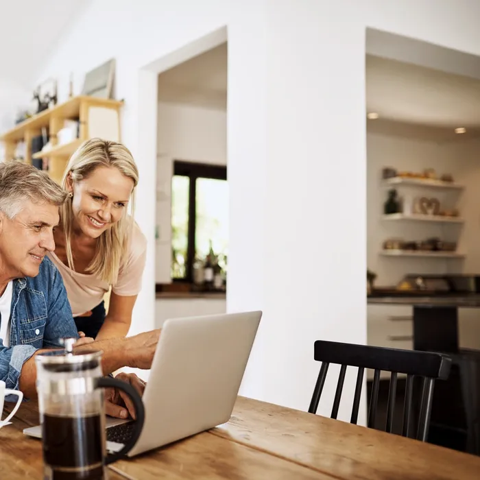 Couple with laptop planning finance, banking and checking retirement budget while becoming debt free at home. Smiling, happy and cheerful