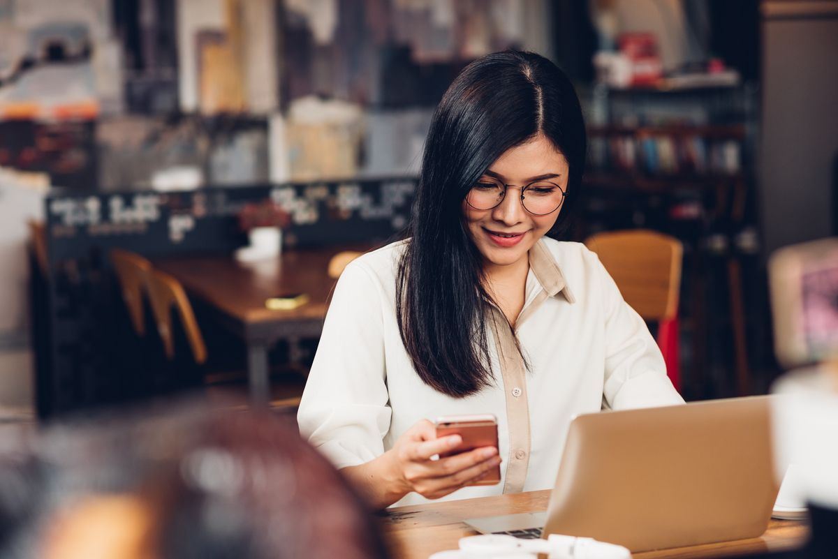 Lifestyle freelance working woman and laptop computer he using smartphone for check status in coffee cafe shop