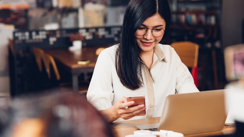 Lifestyle freelance working woman and laptop computer he using smartphone for check status in coffee cafe shop