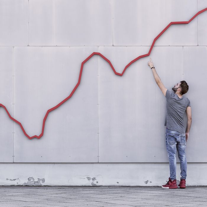 A red bar line graph rises like a financial graph or graphic with a young man pointing at the growth against a wall