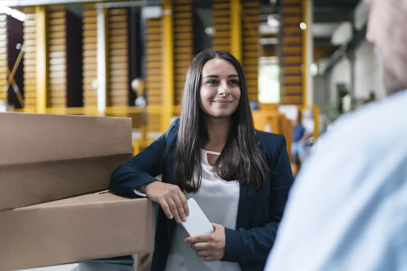 Young woman working in distribution warehouse, talking to colleague