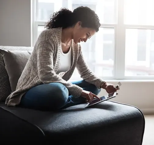 Shot of a cheerful young woman relaxing on a chair while  doing online shopping on a digital tablet at home