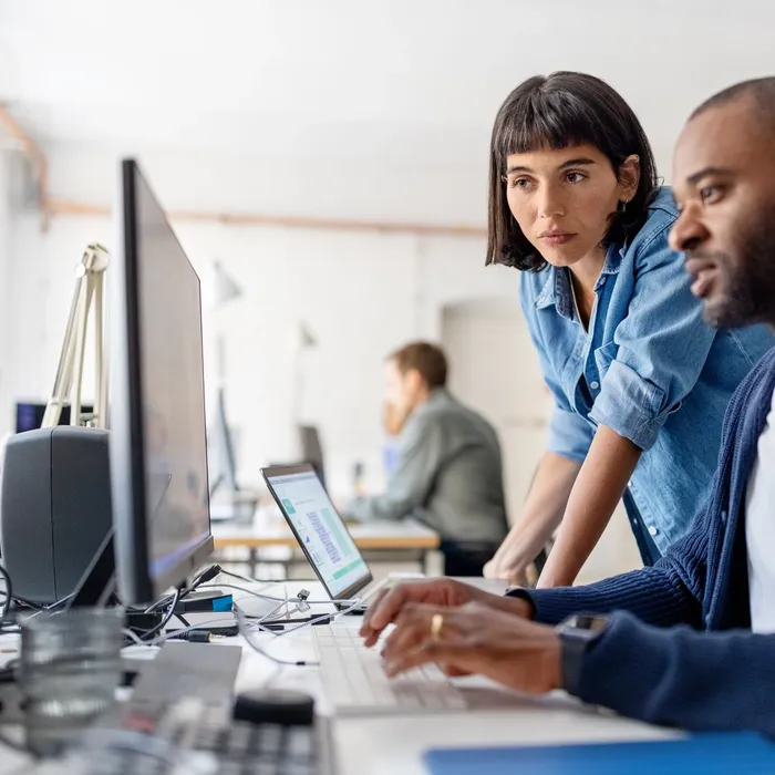 Two business people looking at desktop computer monitor and discussing new programme codes. Male professional working on computer with female colleague standing by looking at computer monitor.Colorful Human