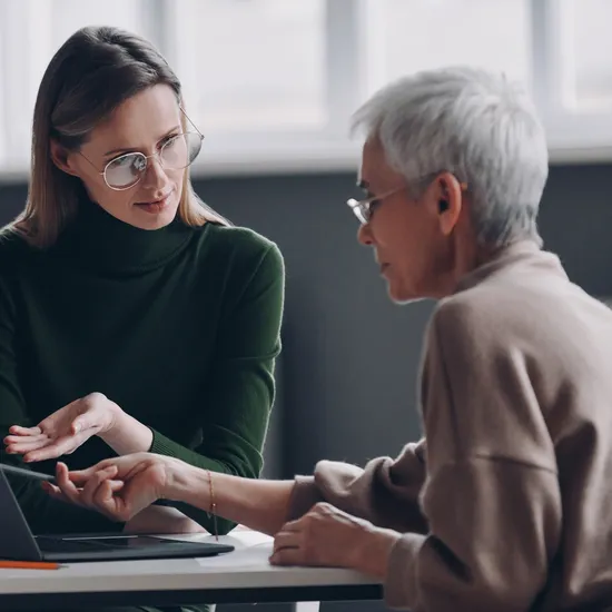 Confident financial advisor pointing laptop while discussing options with senior woman in office