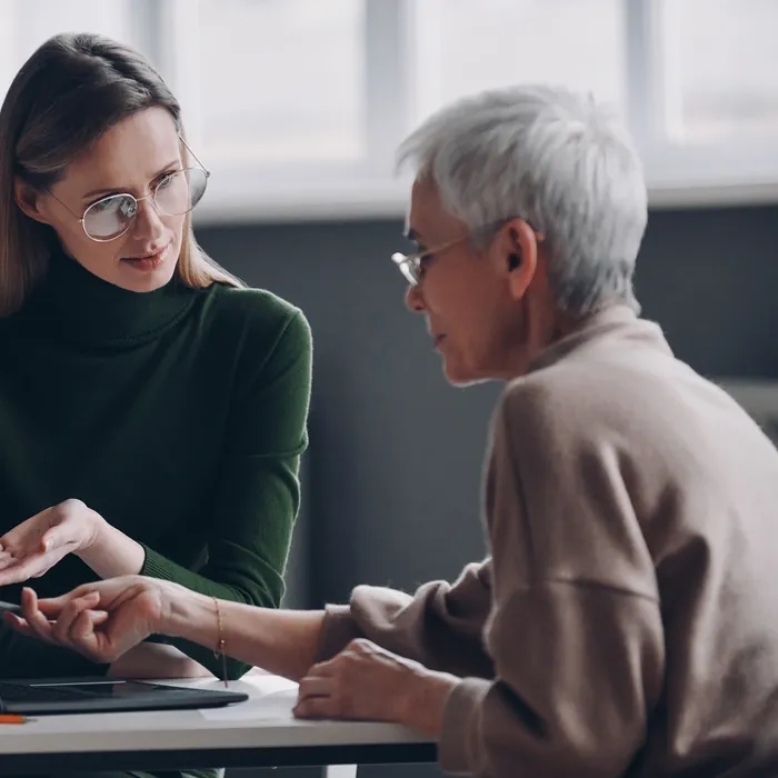 Confident financial advisor pointing laptop while discussing options with senior woman in office