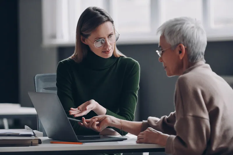 Confident financial advisor pointing laptop while discussing options with senior woman in office