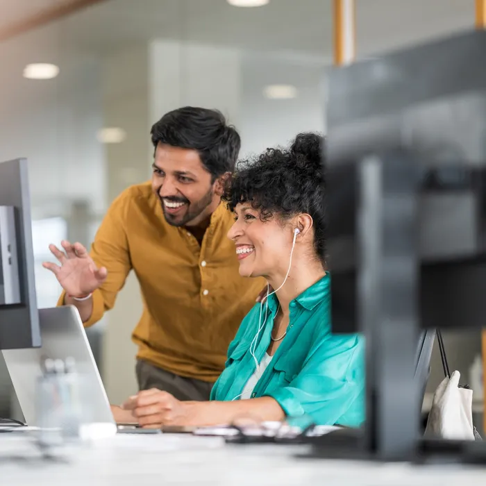 Coworkers in front of computer monitor in modern office chatting online.