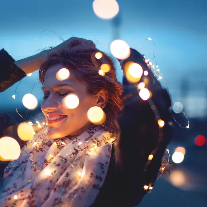 Sensual redhead woman playing with garland fairy lights at night, outdoor in city