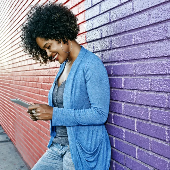 Mixed race woman with cell phone standing by colorful wall