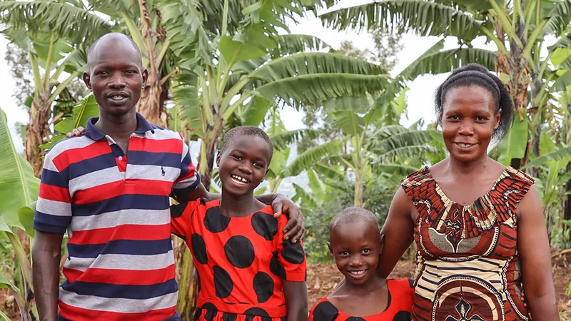 A man, a woman and two children dressed in red are hugging and smiling against a background of trees