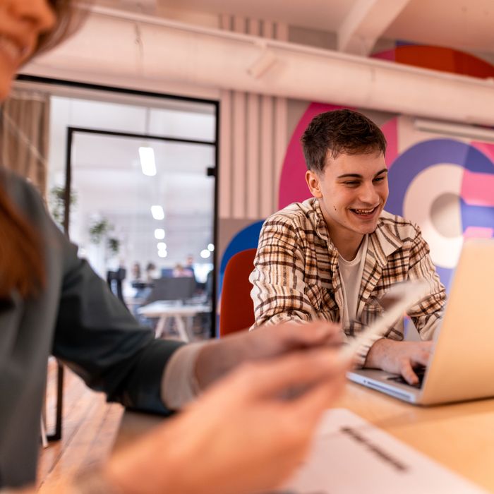 Young man using laptop while working on a project with his colleagues in a modern colorful office, they are smiling and collaborating effectivelyColorful Human