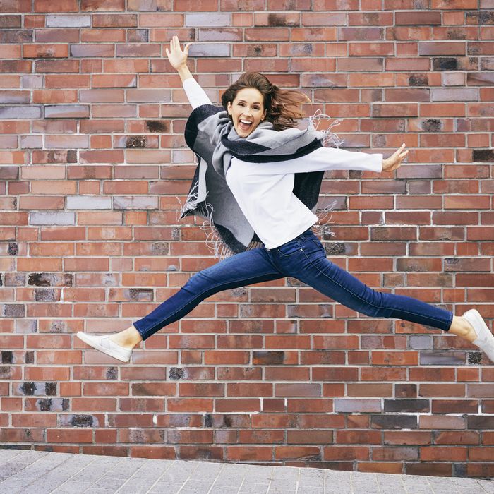 Happy young woman jumping in the air in front of brick wall