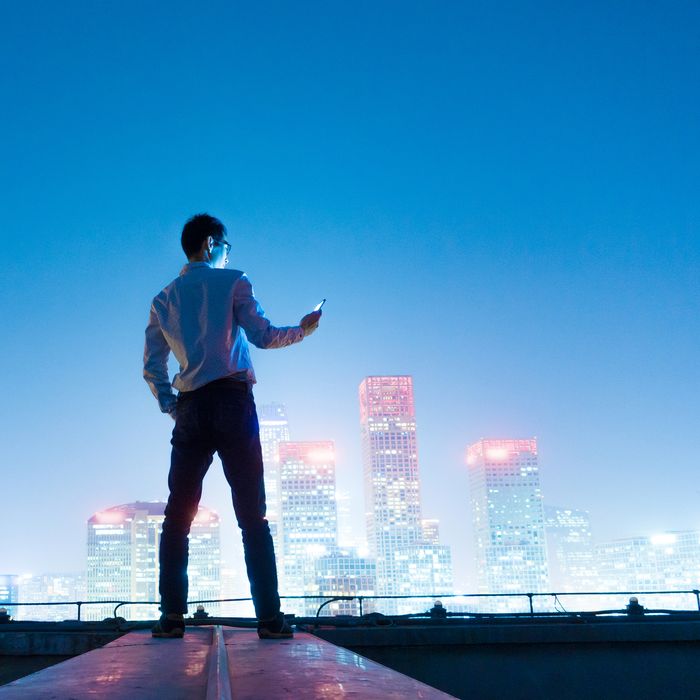 Businessman using smart phone standing on roof with city skyline,Beijing,China