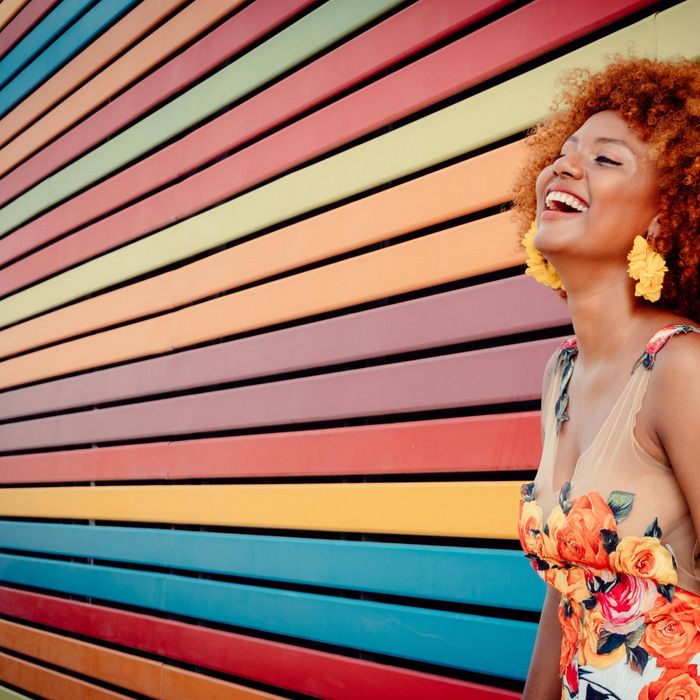 Woman with curly red hair and yellow earrings laughing against a wall of red orange and yellow stripes