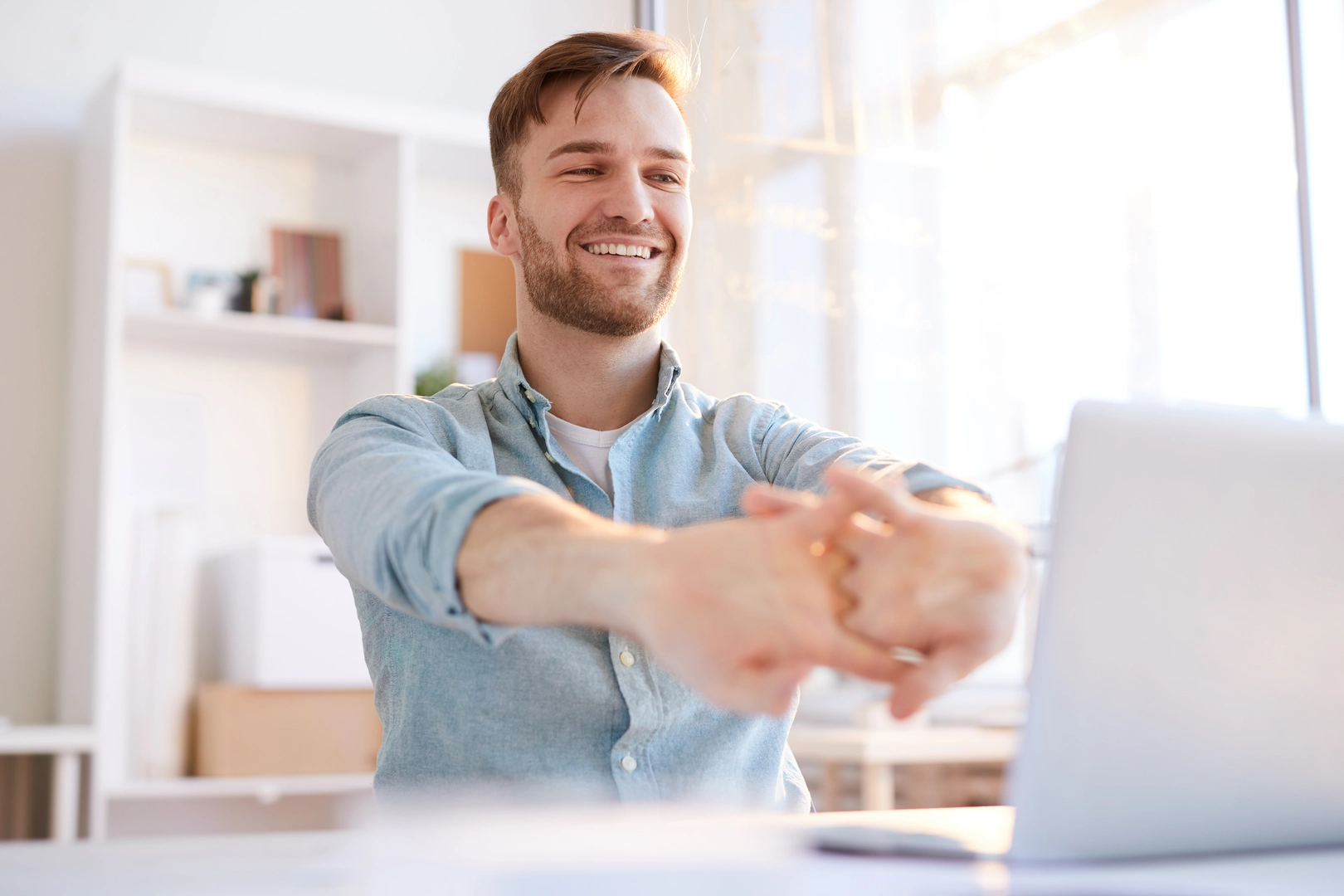 Portrait of handsome young man  stretching at workplace in office and smiling happily, copy space