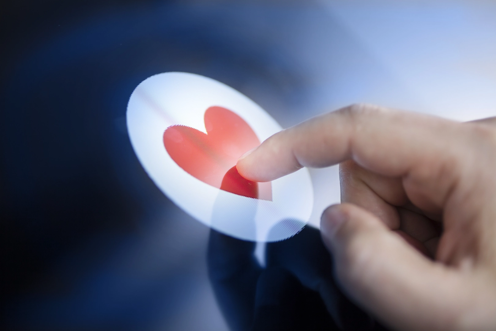 Human finger touching red heart symbol  on a digital display. Dating and and online romance concept