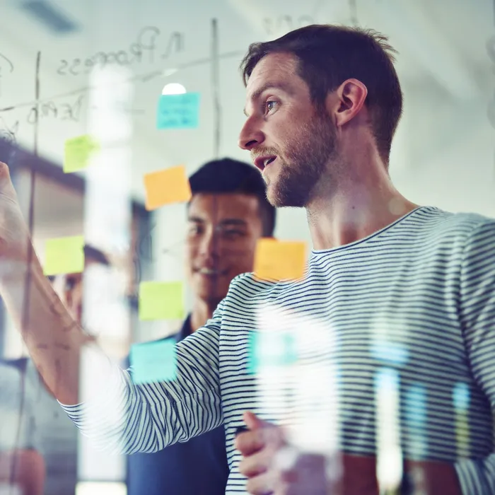 Cropped shot of coworkers using sticky notes on a glass wall during a meeting
