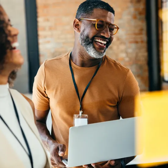 Group of cheerful professionals in a creative office setting, engaged in collaborative work on a digital device, showcasing teamwork and positive energy.