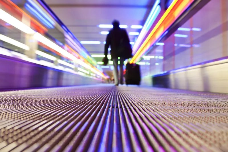 Man walks down the people mover in an airport;