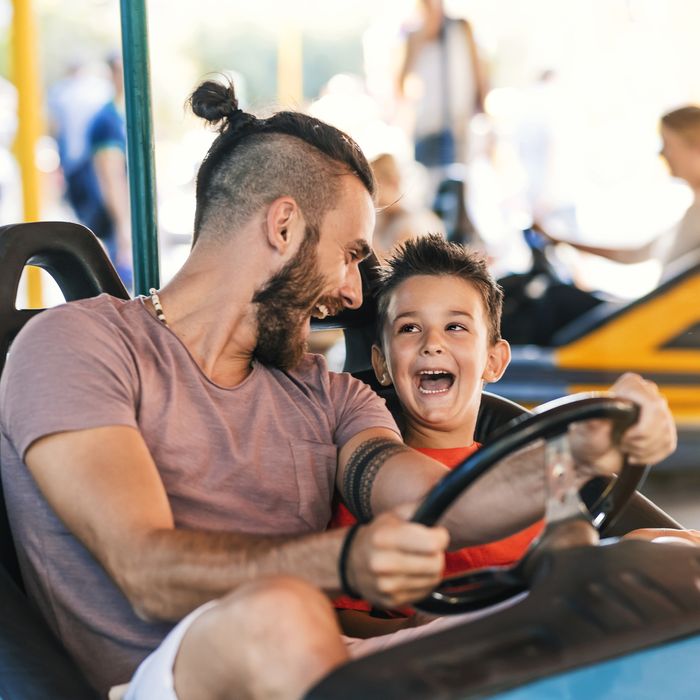 Photo of Caucasian young hipster Father and his 5 years old son having a ride in the bumper car at the amusement park during summer day. Happy family leisure in holiday weekend
