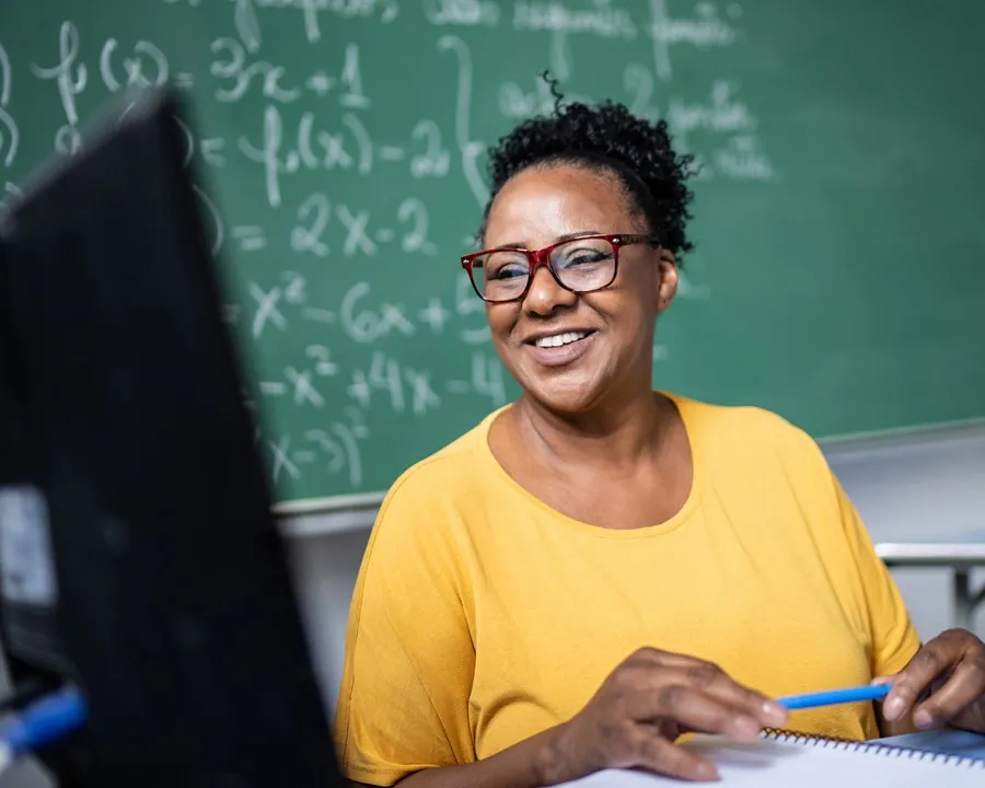 smiling woman with pen in her hands looking at a PC monitor