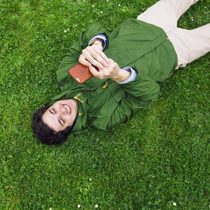Young happy man lying on the grass and using smart phone