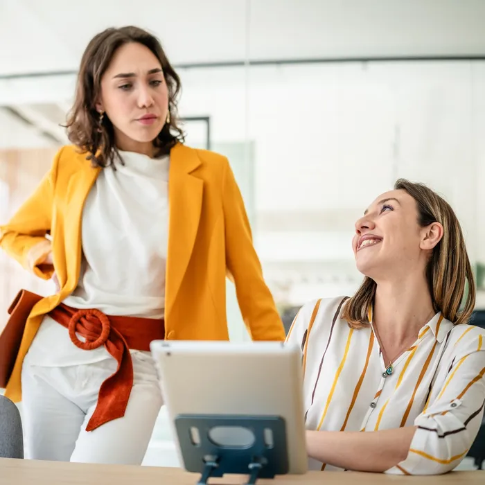 Two young businesswomen are smiling and discussing ideas in a bright, contemporary office.Colorful Human